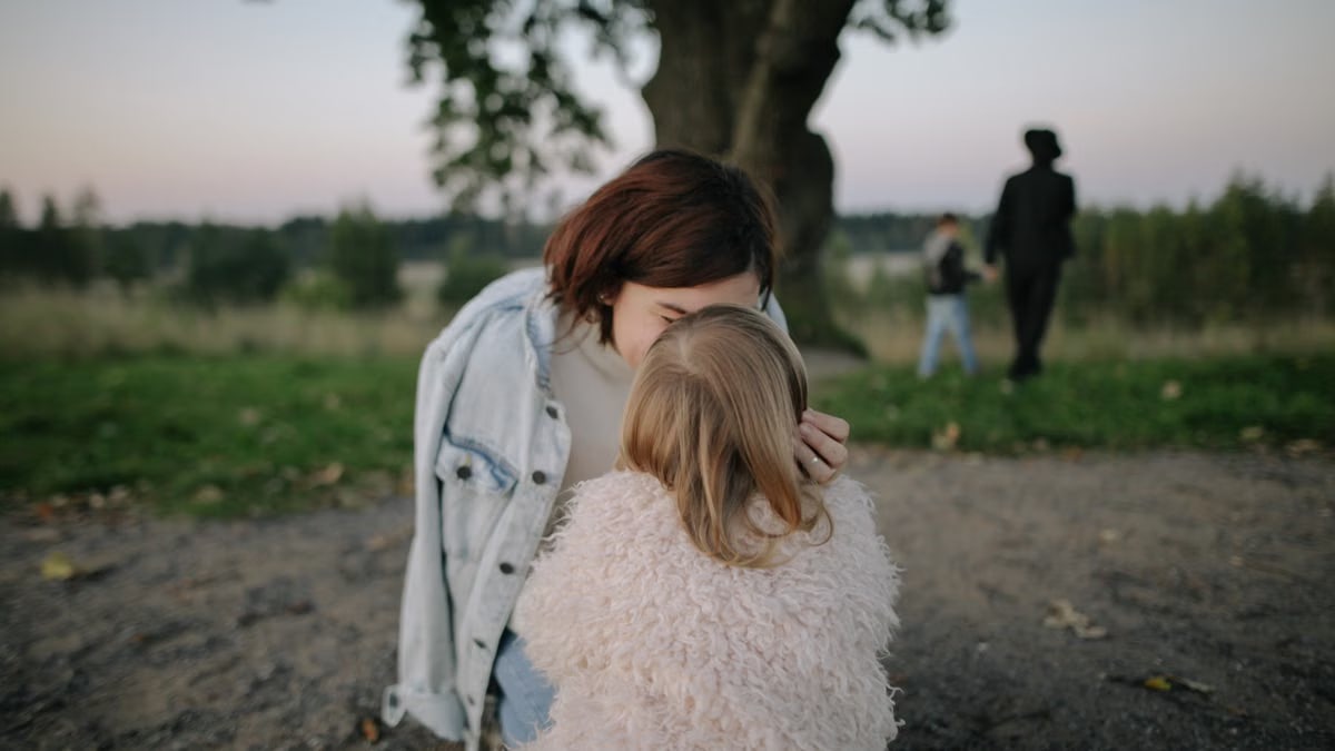 A tender moment between mother and daughter outdoors in a grassy field at twilight.